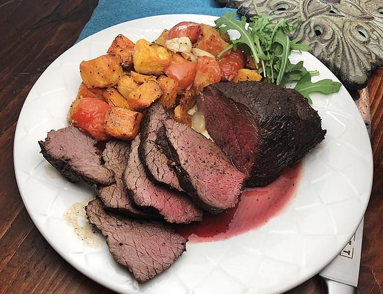 Elk Recipes & Wild Game Cooking Ideas - Roasted elk top sirloin sliced on a serving platter with herbs 